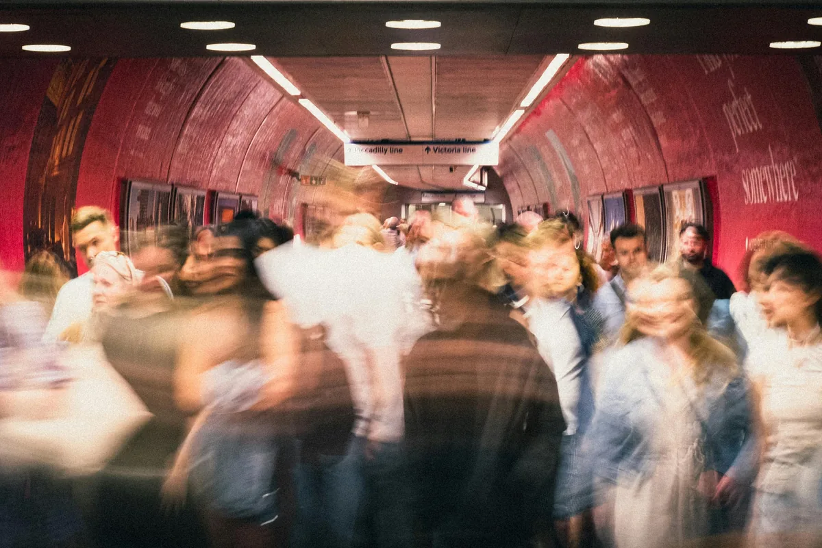 A dense, motion-blurred crowd moving through a Piccadilly and Victoria line interchange tunnel during the rush
