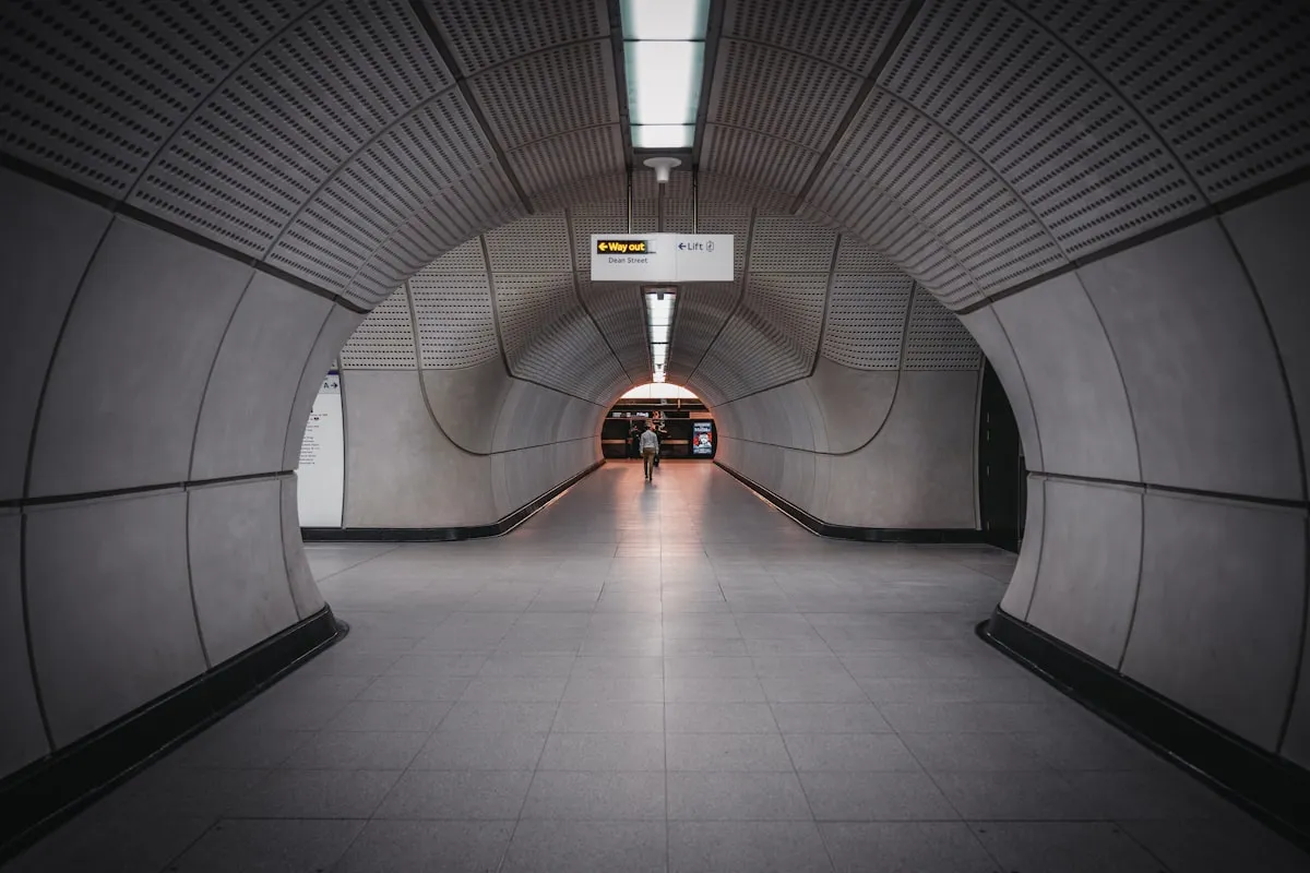 A passenger walks through a circular Elizabeth line tunnel at Tottenham Court Road, the smooth concrete bore of a tunnel-boring machine visible in the walls and ceiling